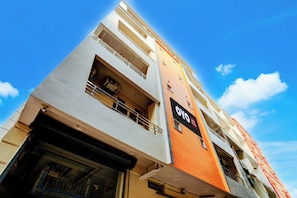 Un edificio de hotel de varios pisos con balcones, un letrero que indica que es un hotel OYO, y un cielo azul despejado al fondo.