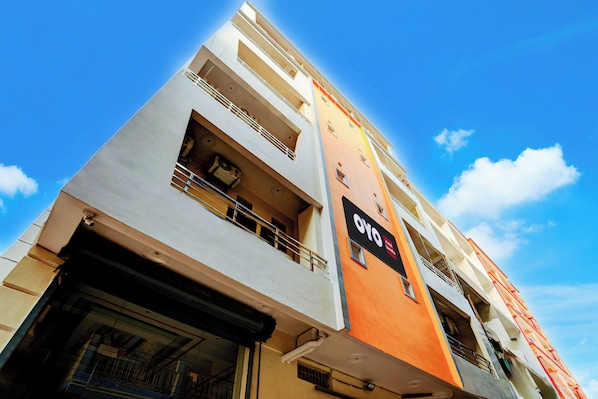 Un edificio de hotel de varios pisos con balcones, un letrero que indica que es un hotel OYO, y un cielo azul despejado al fondo.