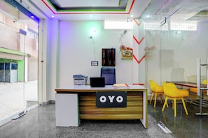 Una oficina moderna con un mostrador de recepción identificado como 'OYO', una impresora, un ordenador y un panel de vidrio.