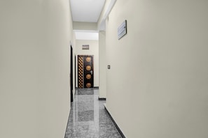 Un pasillo con una puerta al final, un interruptor de luz en la pared y una pequeña ventana sobre la puerta.