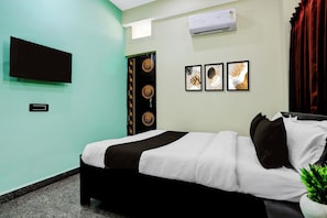 Una habitación de hotel con una cama, un televisor de pantalla plana montado en la pared, un equipo de aire acondicionado y tres obras de arte enmarcadas.
