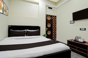 Una habitación de hotel con una cama grande, un televisor montado en la pared y una mesita con una tetera y tazas.
