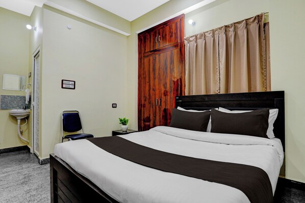A bedroom with a bed, a nightstand, a wooden wardrobe, a bathroom with a sink, and a shower.