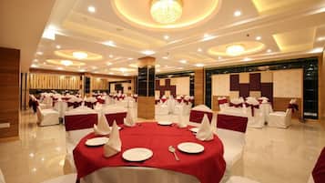 Un salón de banquetes con mesas redondas dispuestas para comer, sillas blancas con cintas rojas y una lámpara de araña moderna.
