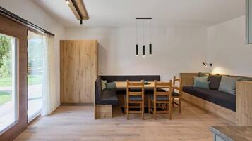Un intérieur moderne avec une table à manger en bois, des chaises, un canapé et un banc. On y trouve également un mur d’accent en bois et un luminaire suspendu.