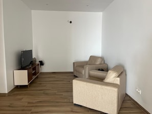 A living room with a flat-screen TV on a wooden stand, a beige sofa, and a wooden floor. - Perfect 3-bedroom apartment in Praia for a relaxing getaway (Praia)