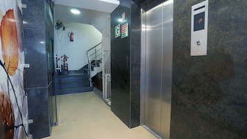Un ascensor con señalización de salida de emergencia, un extintor y una escalera con barandilla.