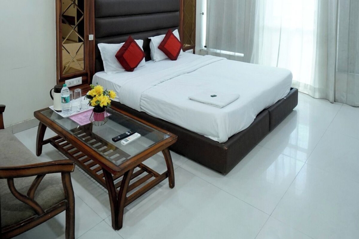 A hotel room with a bed, a bedside table, a chair, a ceiling fan, and a window with curtains.