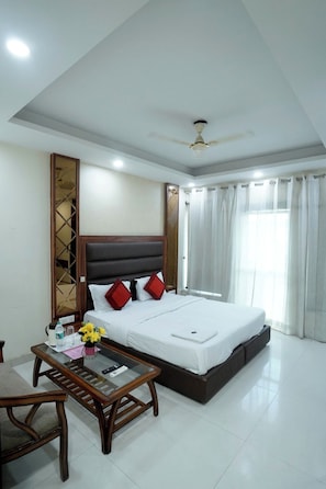 A hotel room with a bed, a bedside table, a chair, a ceiling fan, and a window with curtains.