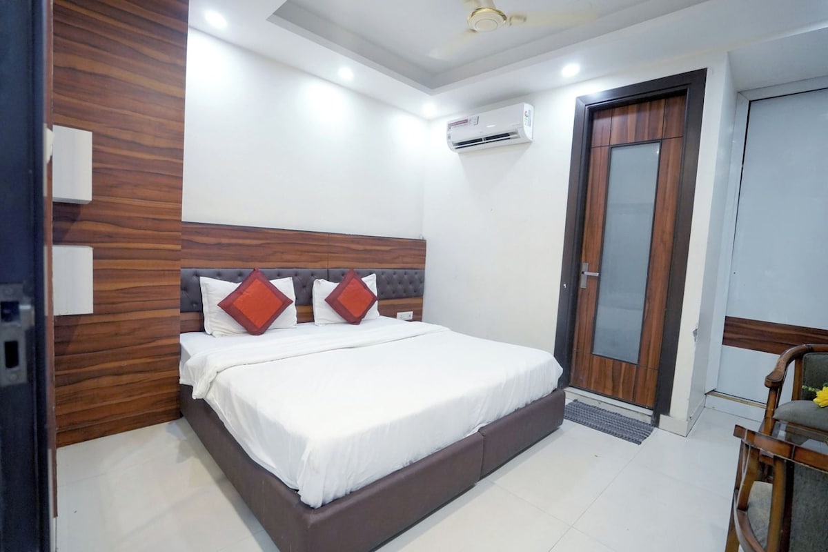 A bedroom with a bed, wooden headboard, white bedding, and an air conditioning unit.