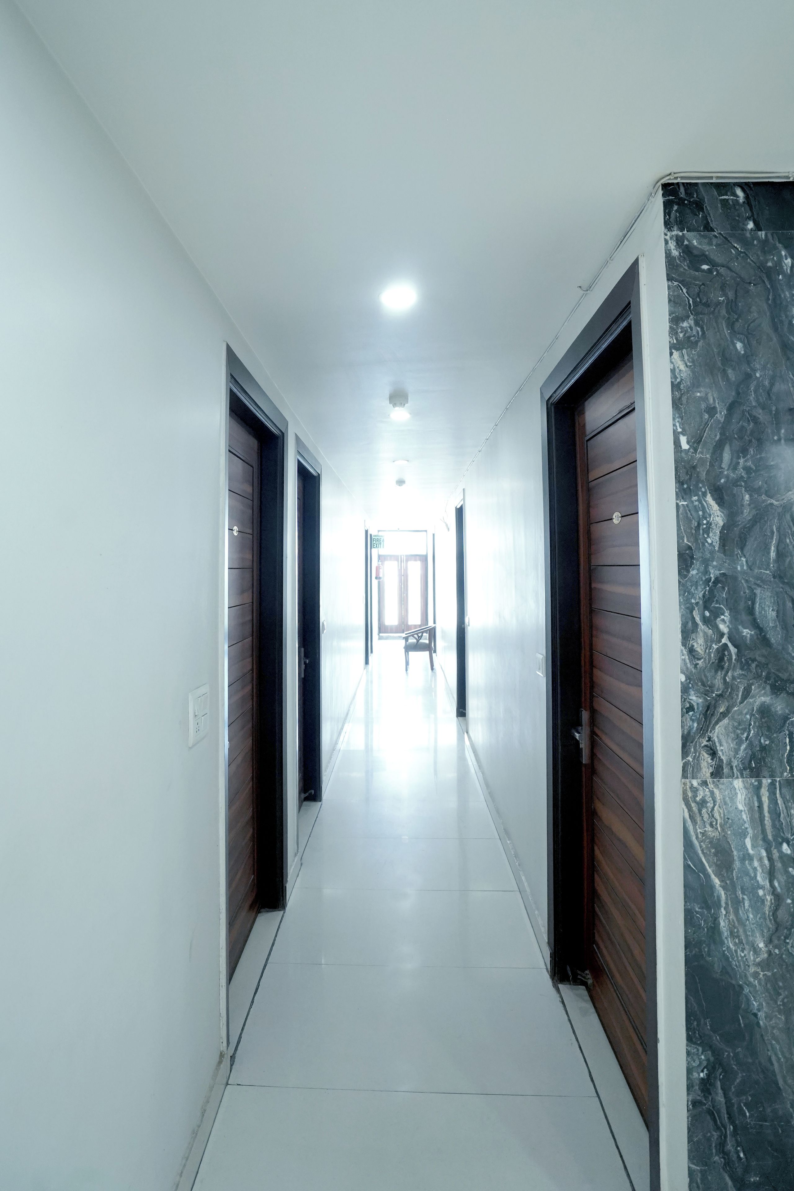 A corridor with doors on both sides, a white tiled floor, and a ceiling light.