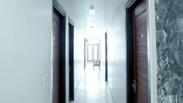 A corridor with doors on both sides, a white tiled floor, and a ceiling light.