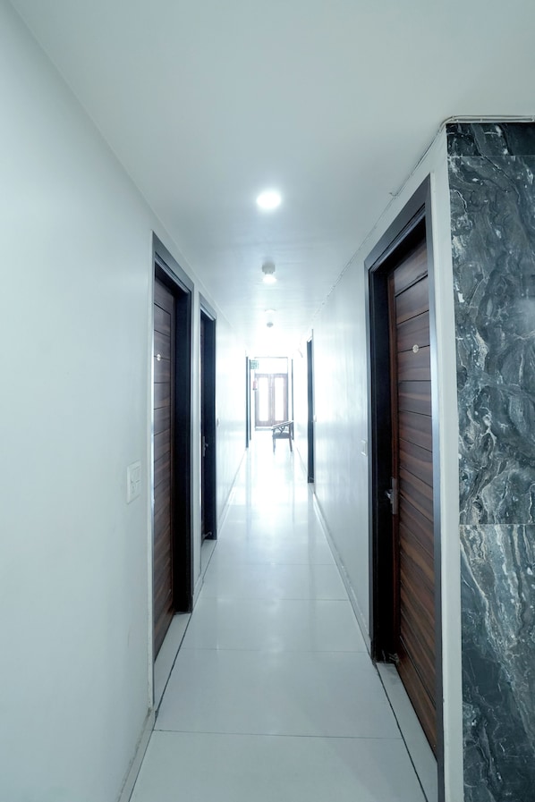 A corridor with doors on both sides, a white tiled floor, and a ceiling light.
