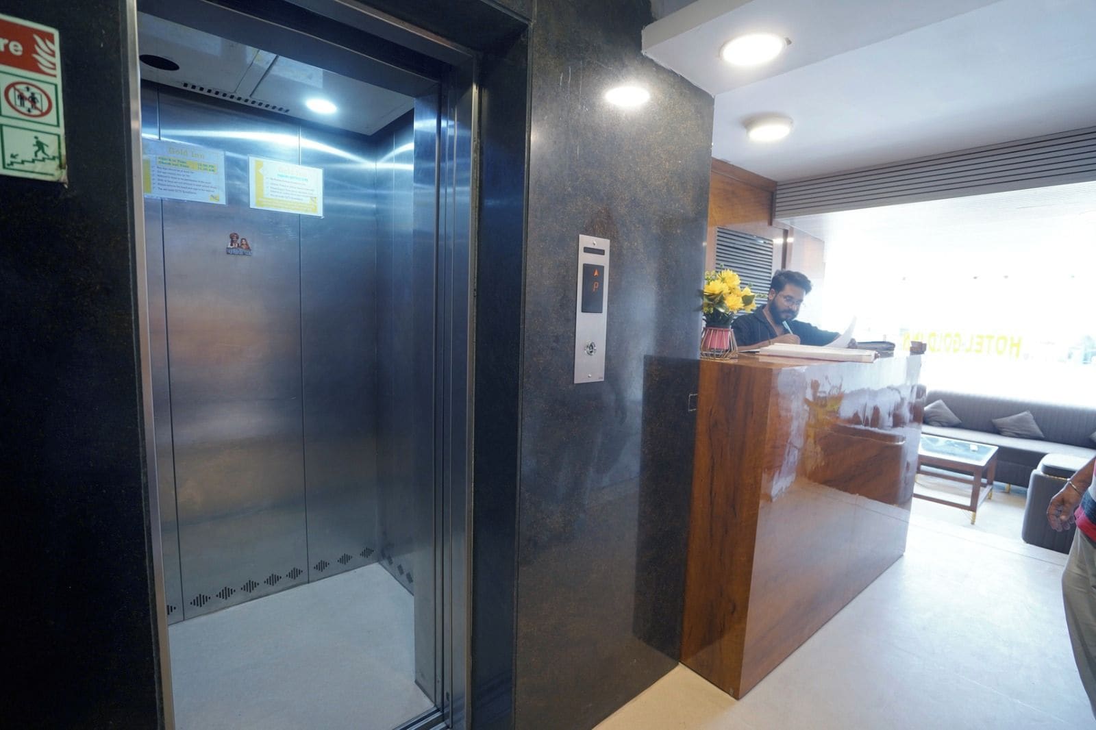 Een lift met een metalen inrichting en een receptiebalie met een vaas gele bloemen.
