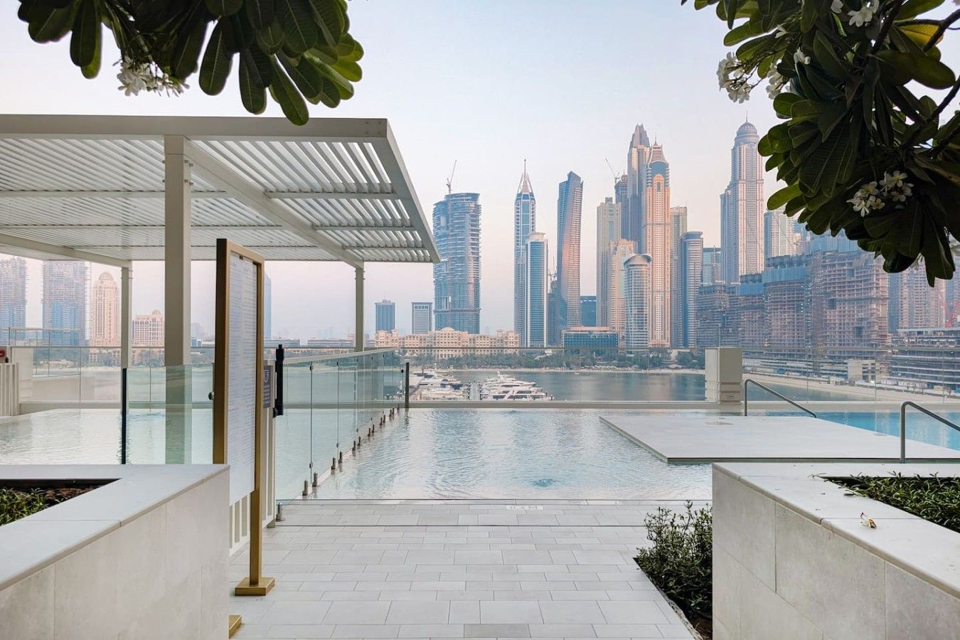 A rooftop infinity pool with a city skyline view, a covered seating area, and a clear sky.