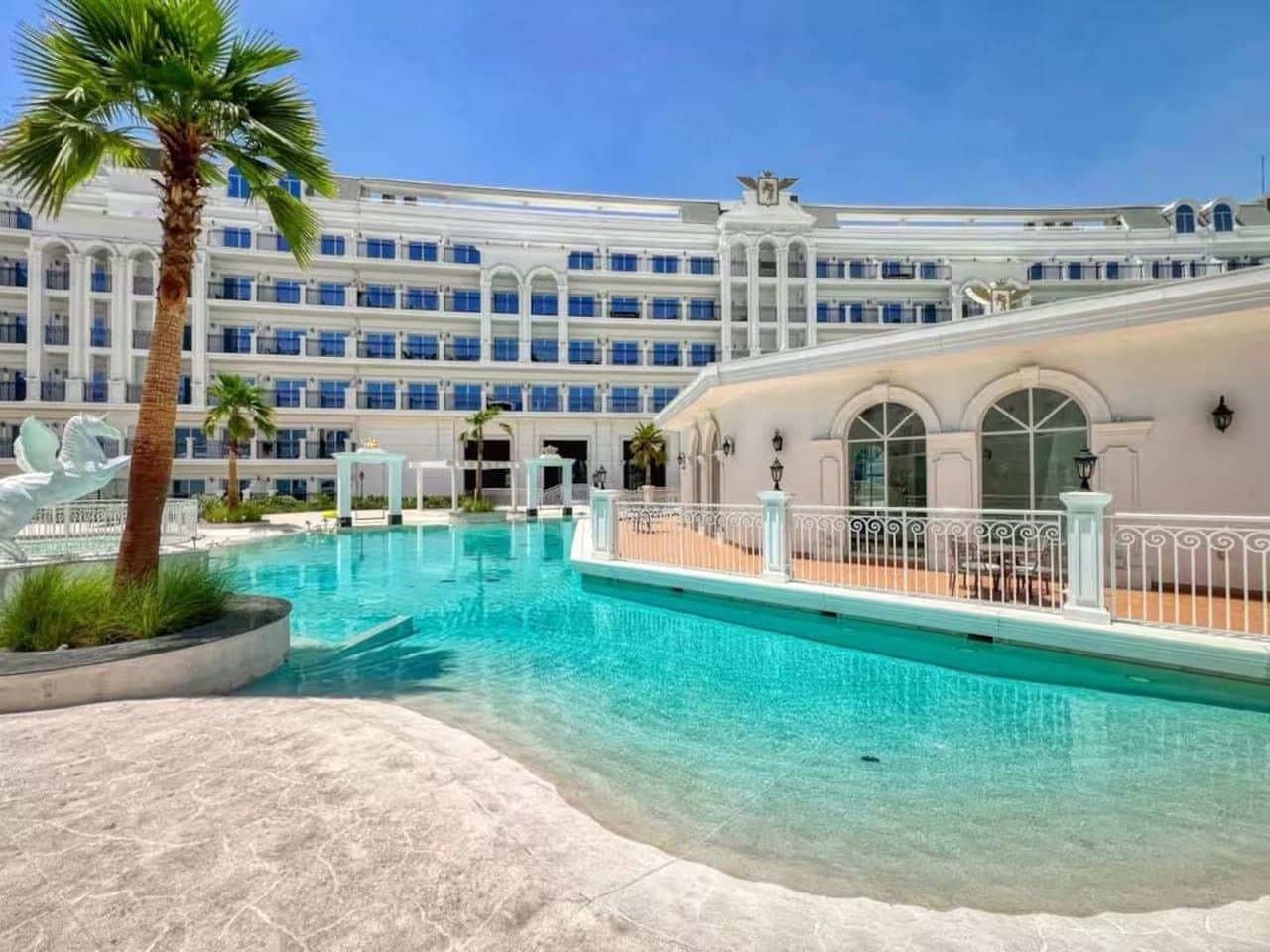 Ein Hotel mit großem Pool, Palmen und einem mehrstöckigen Gebäude mit Balkonen.
