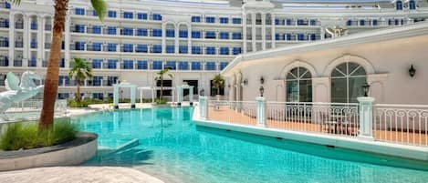 Ett hotell med en stor pool, palmer och en flervåningsbyggnad med balkonger.