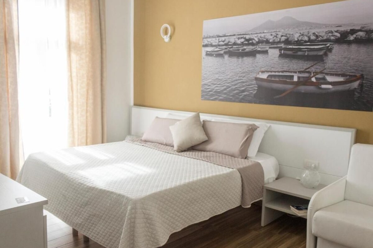 Una camera d'albergo con un letto, un comodino, una sedia e una tazza da caffè attaccata al muro.