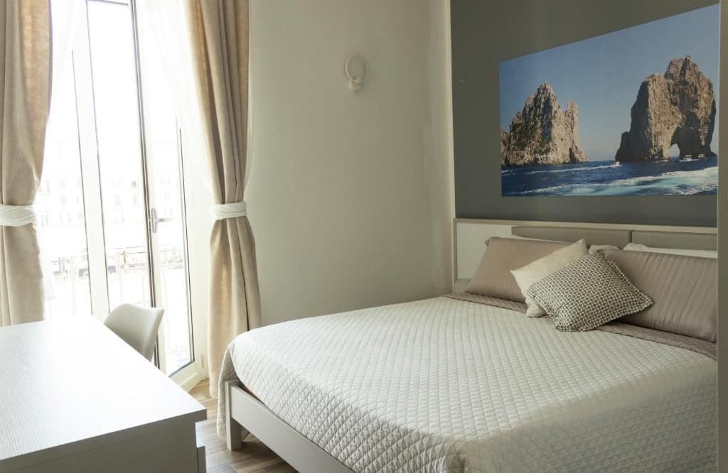 A bedroom with a bed, a desk, and a large window with curtains.