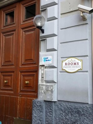 Eine Gebäudefassade mit einer Holztür, einer Straßenlaterne, einem Schild mit der Aufschrift 'Global Broker Rooms' und einer Plakette mit der Bezeichnung 'Stazione Centrale 3. Stockwerk'.