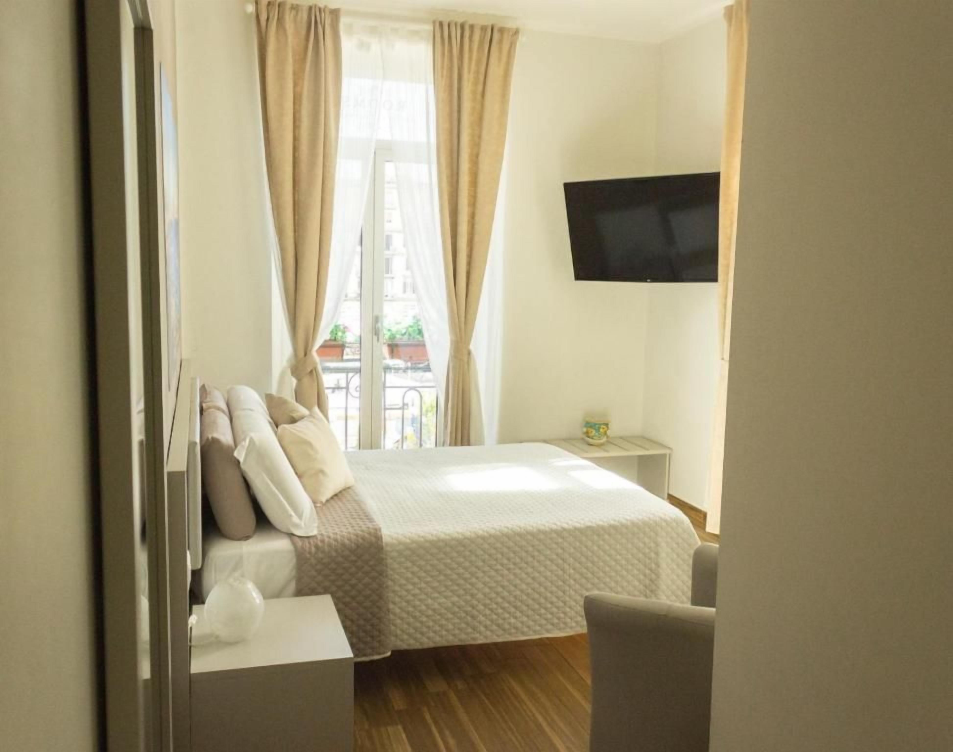 Ein Hotelzimmer mit einem Bett, einem Fernseher, einem kleinen Tisch und einem Fenster mit Vorhängen.