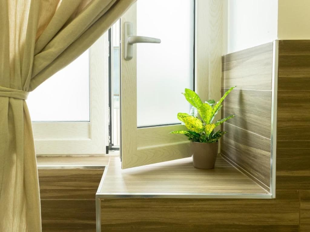 Une pièce avec un plancher en bois, une fenêtre avec des rideaux et une plante en pot posée sur une étagère en bois.