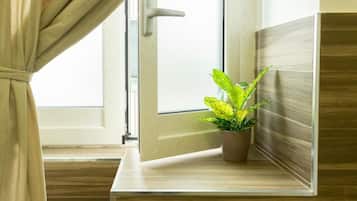Una habitación con piso de madera, una ventana con cortinas y una planta en maceta sobre un repisa de madera.