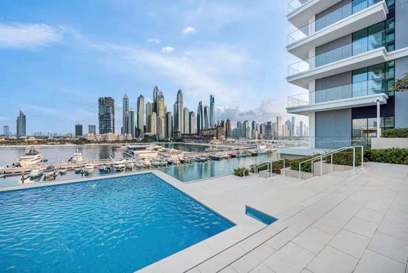 Ein modernes Gebäude mit Pool auf dem Dach, mit Blick auf einen Hafen voller Boote und eine Stadtansicht.
