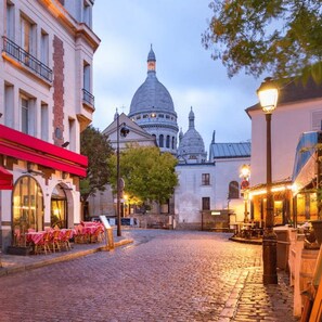 A cobblestone street leading to a historic building with domed architecture. - The Montmartre 1881 (Paris)