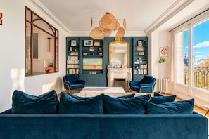 Ein Wohnzimmer mit einem blauen Sofa, zwei Sesseln, einem Kamin und einem großen Fenster mit Ausblick.