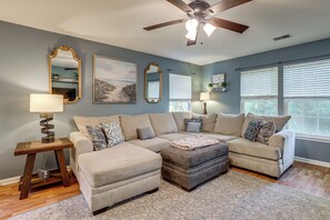 A living room with a sectional sofa, a ceiling fan, and a large window with blinds. - Golf + Pool Fun! Family Condo 6 Mi to Myrtle Beach (Myrtle Beach)