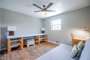 Ein Schlafzimmer mit einem Bett, einem Schreibtisch, einem Stuhl, einem Deckenventilator und einem Fenster.