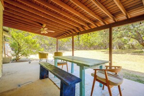 Eine überdachte Terrasse im Freien mit einem Holztisch und Bänken, umgeben von Bäumen.