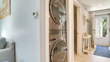 A laundry room with two front-loading washing machines, a small table with a candle, and a door leading to a hallway.
