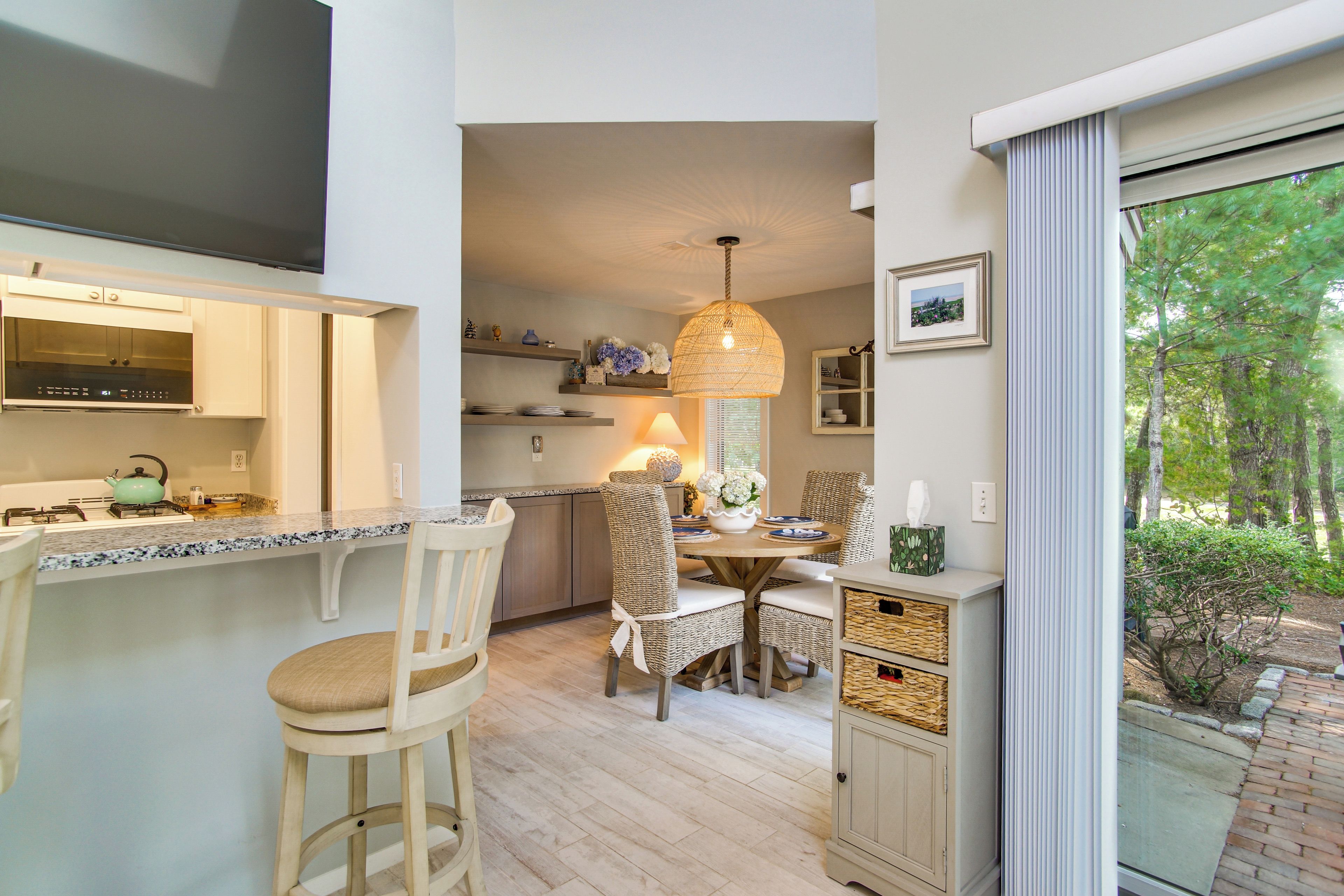 A kitchen with a built-in oven, a dining area with a table and chairs, and a view of the outdoors through a window.