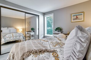Ein Hotelzimmer mit einem großen Bett, einem Schreibtisch, einem Sessel und einem Spiegel, sowie einem Fenster mit Jalousien.