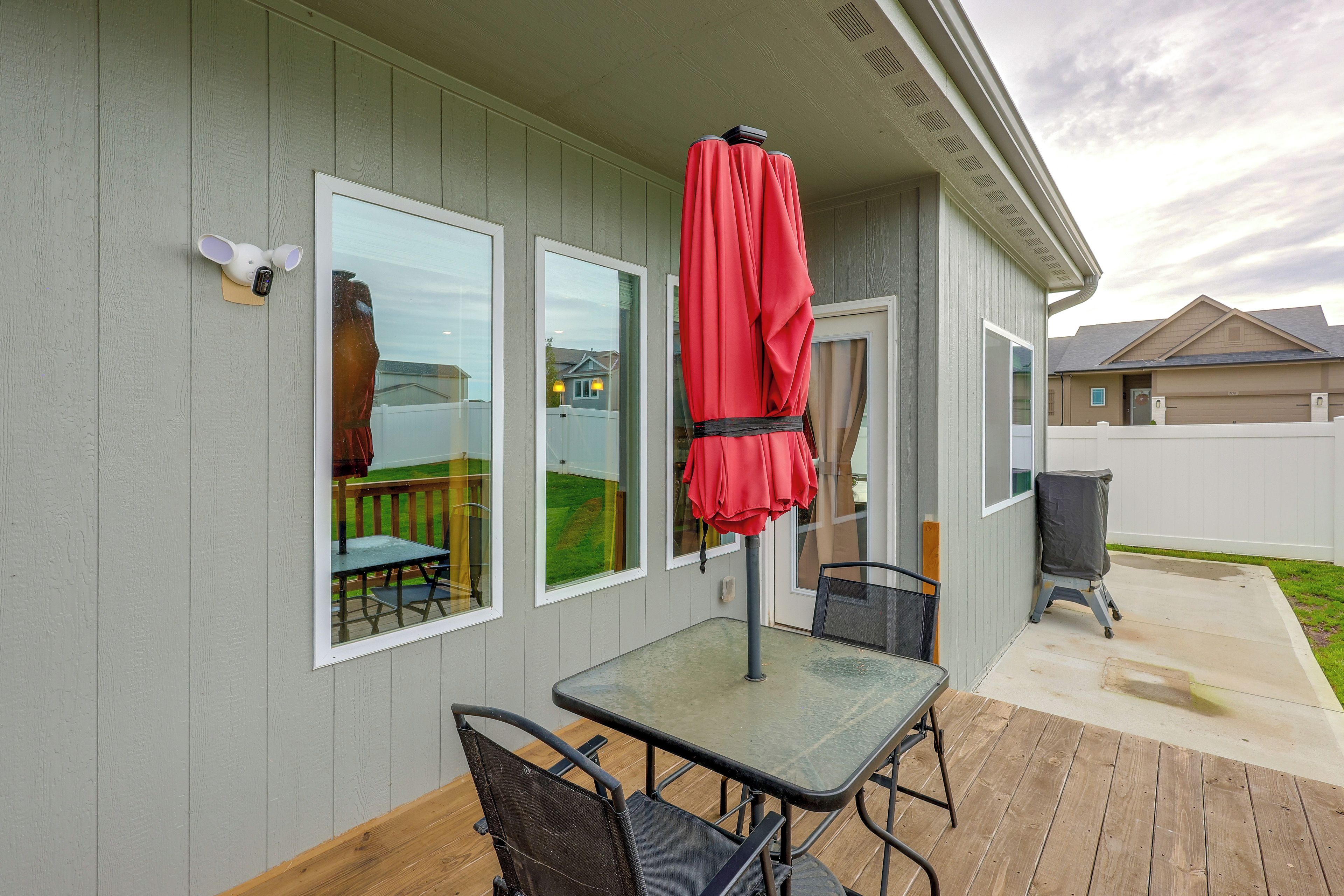 A patio with a table and chairs, a red umbrella, and a security camera on the wall.