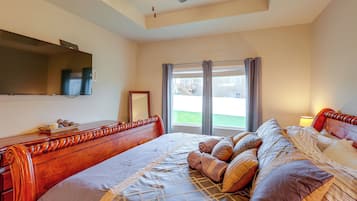 A bedroom with a large bed, a flat-screen TV, a ceiling fan, and a window with curtains.
