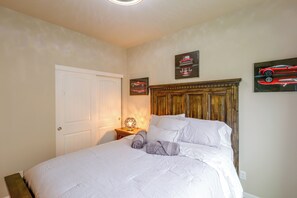 A bedroom with a wooden headboard, a bed with white bedding, a nightstand with a lamp, and two framed pictures on the wall.