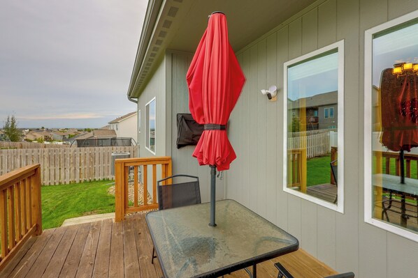 A deck with a table and a red umbrella, a wooden fence, and a view of a residential area.