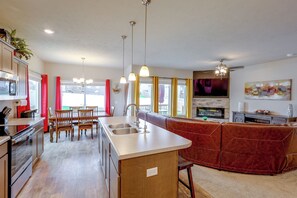 A modern kitchen with a central island, dining area with chairs, and a living space with a sofa and entertainment unit.