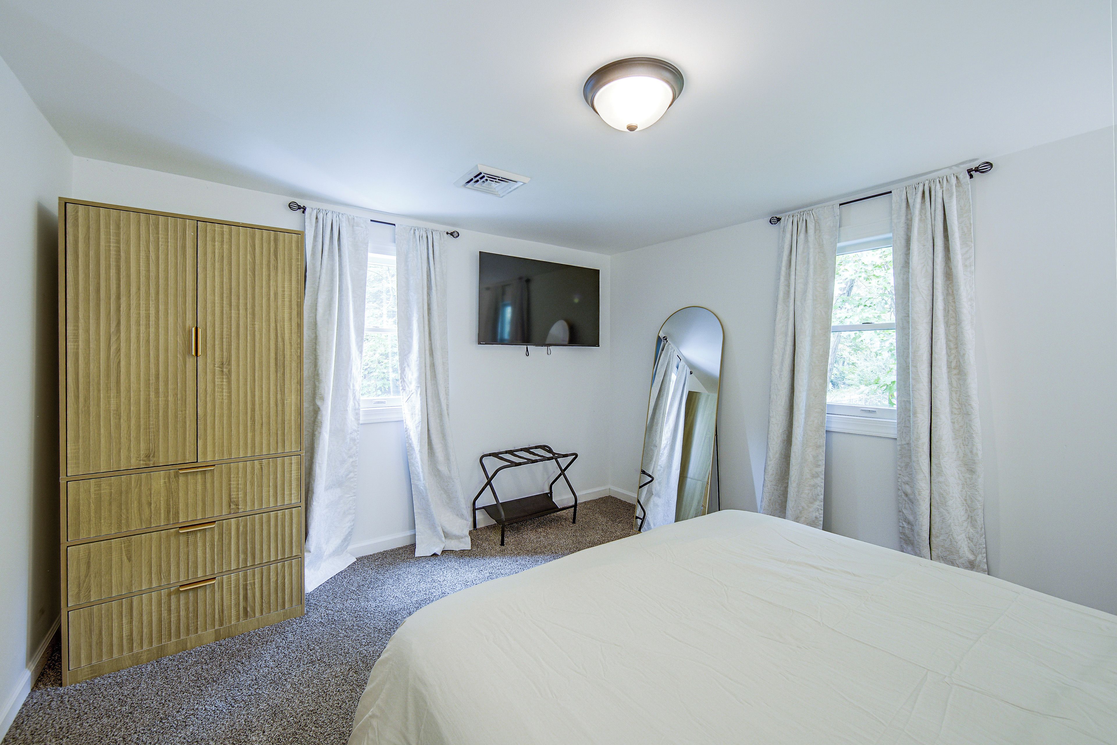 Un dormitorio con cama, armario, espejo y ventana con cortinas.