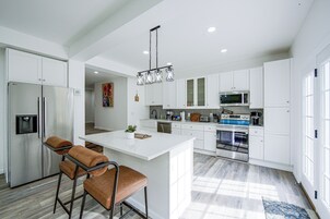 Una cocina moderna con armarios blancos, electrodomésticos de acero inoxidable y una isla central con asientos.