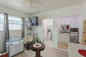 A compact living space with a kitchenette, a television mounted on the wall, a small round table, and a chair. - 2 Mi to Universal Orlando! Quiet Studio Suite (Orlando)