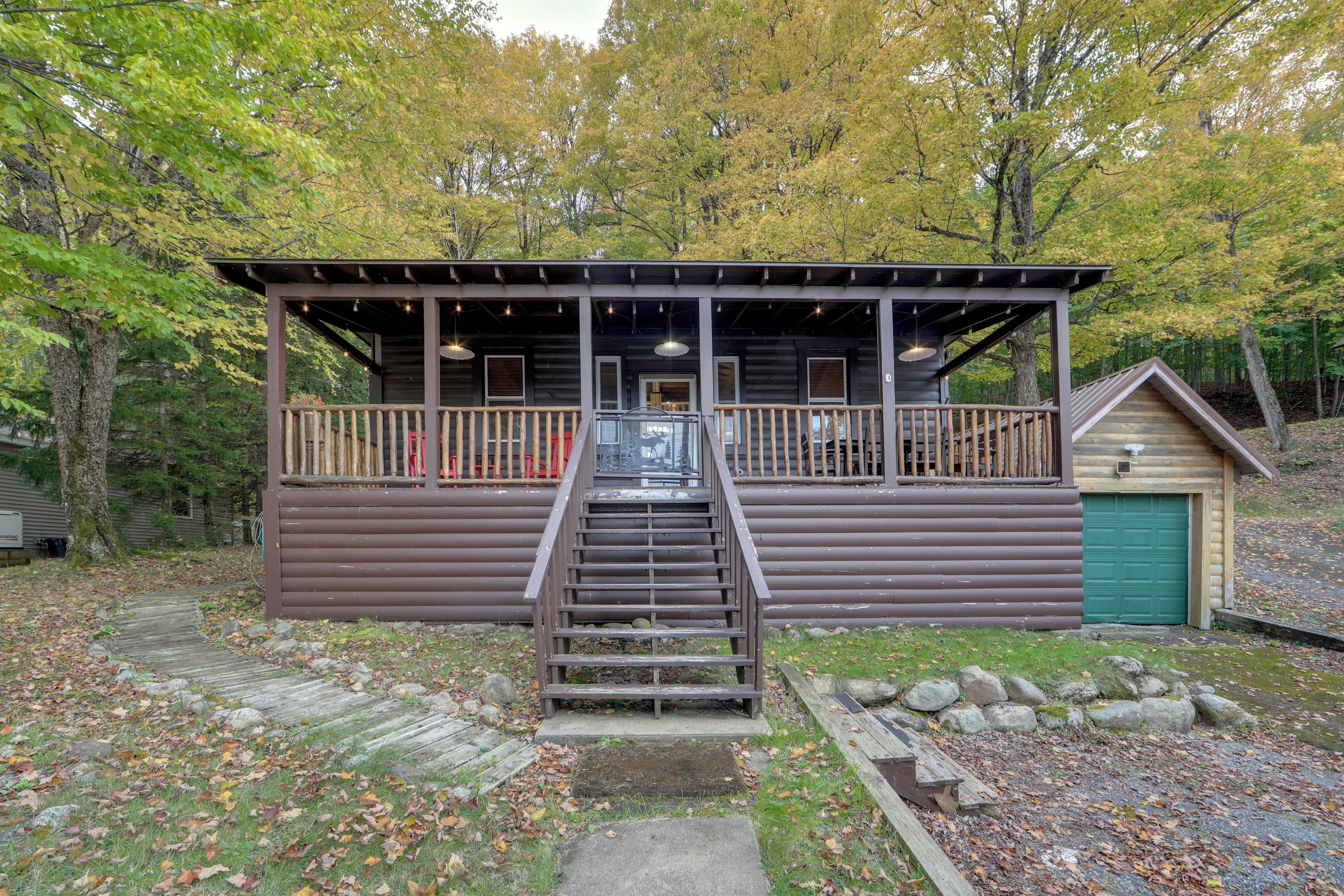 A cabin with a wooden deck, a staircase leading to a covered porch, and a green garage door.