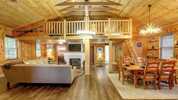 A spacious cabin interior with a loft bedroom, a dining area, and a fireplace.
