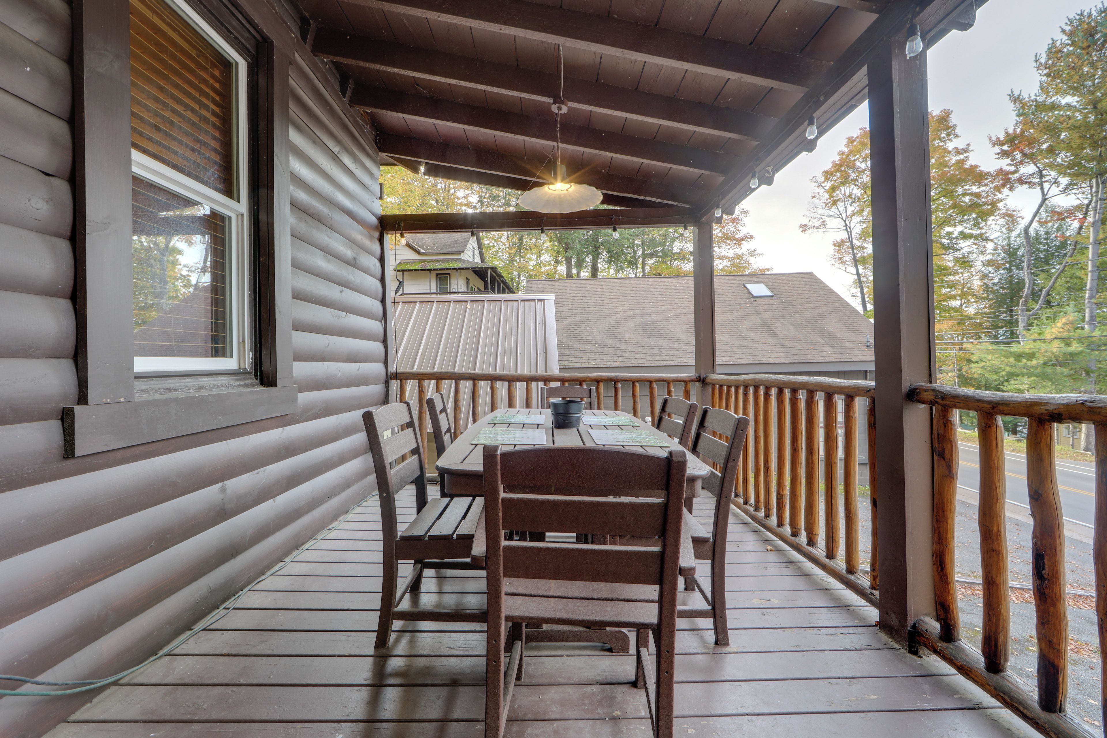 A covered outdoor dining area with a table and chairs, a wooden railing, and a view of a house in the background.