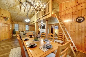 A wooden interior with a dining table set for four, a staircase, and a bear-themed clock.
