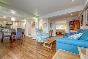 A spacious living room with a blue sofa, a dining area with chairs, and a kitchen in the background. - Walk to Downtown Edmonds! Condo w/ Patio (Edmonds)