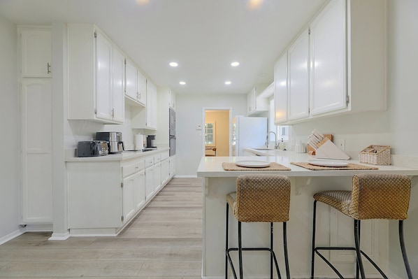 A modern kitchen with white cabinetry, a central island with bar stools, and a visible door leading to another room. - 1 Mi to Dtwn Downey + Fenced Yard! (Downey)